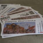 Stos wizytówek z nazwiskiem Justyna Wojnowska, obrazem starego europejskiego miasta i danymi kontaktowymi, w tym adresem e-mail, numerem telefonu i ikonami mediów społecznościowych.