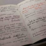 Otwarty notatnik ze stronami wypełnionymi odręcznym pismem w języku polskim, z różnymi stylami pisma, czarnym i czerwonym atramentem oraz podkreślonymi słowami. Notatnik leży na neutralnej powierzchni.