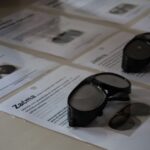 Para czarnych gogli symulacyjnych spoczywa na stole na wydrukowanych arkuszach informacyjnych zawierających tekst i obrazy. W tle widoczna jest kolejna para gogli i więcej dokumentów.