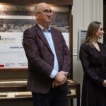 Mężczyzna w kraciastej marynarce i kobieta w sukience w kropki stoją obok siebie w pomieszczeniu, przed gablotą z napisem Mirabilia Collectio.